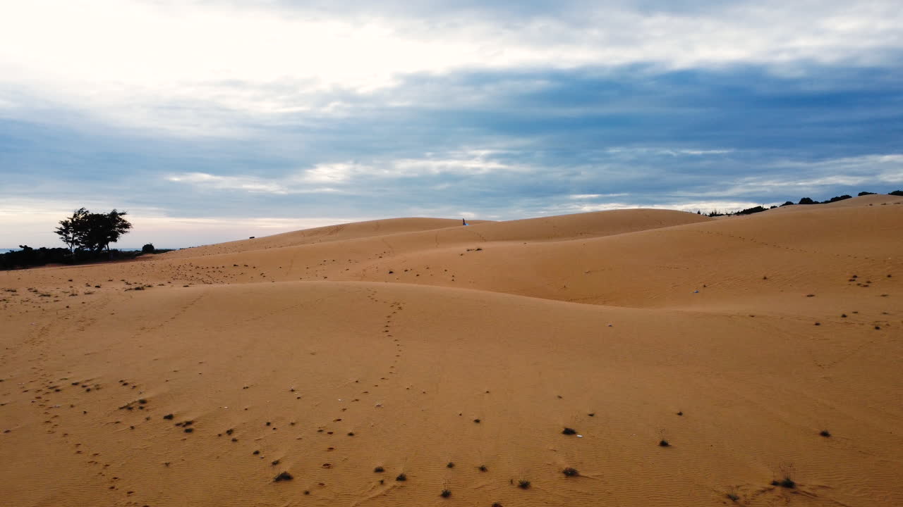 vista aérea hacia delante de las dunas de arena roja con un ambiente atemporal y una chica corriendo a lo lejos
