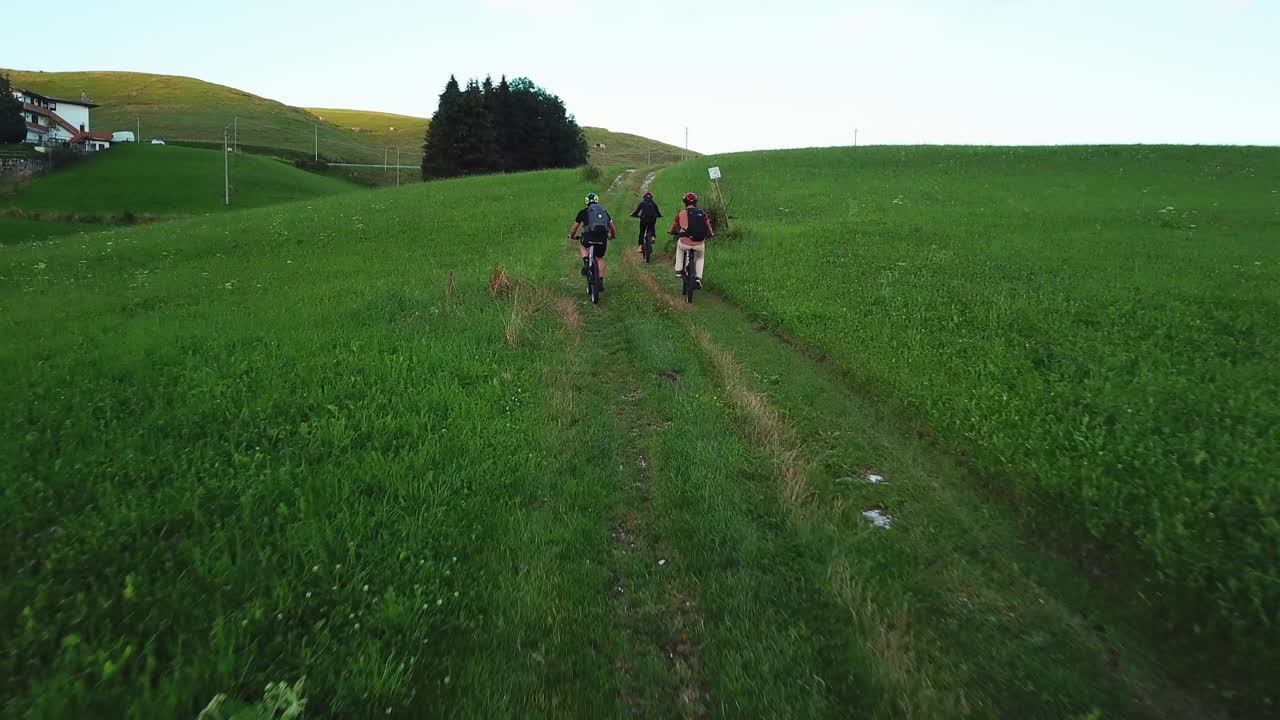 People participating in off road sports activities in the countryside. Aerial back view following a group of mountain bikers driving the bicycles uphill