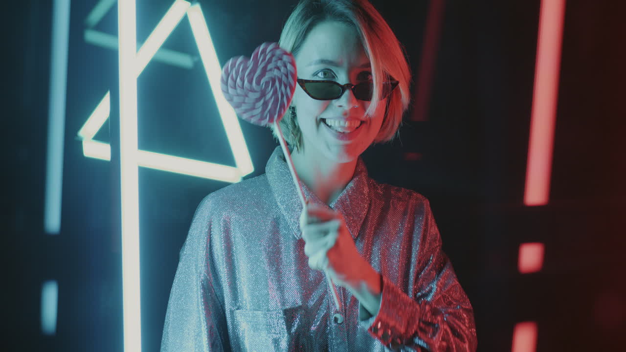 Stylish woman with lollipop under vibrant neon lights