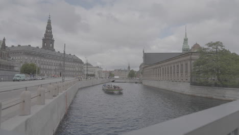 christianborg building in copenhagen wide view over the river while a boat is passing on a cloudy day log