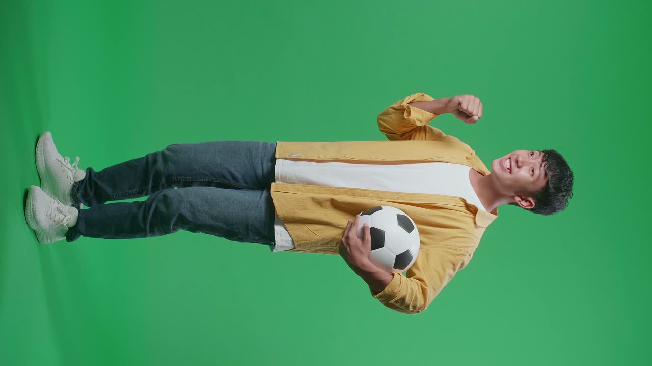 흥분 된 아시아 소년의 전체 몸 측면 뷰 공은 녹색 화면 배경에서 축구를 응원하는 동안 골에 총을 기 위해 니다