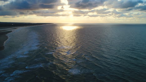 stunning beautiful golden hour sunset over the sea with small waves breaking at the shoreline with sandy beach high aerial drone shot