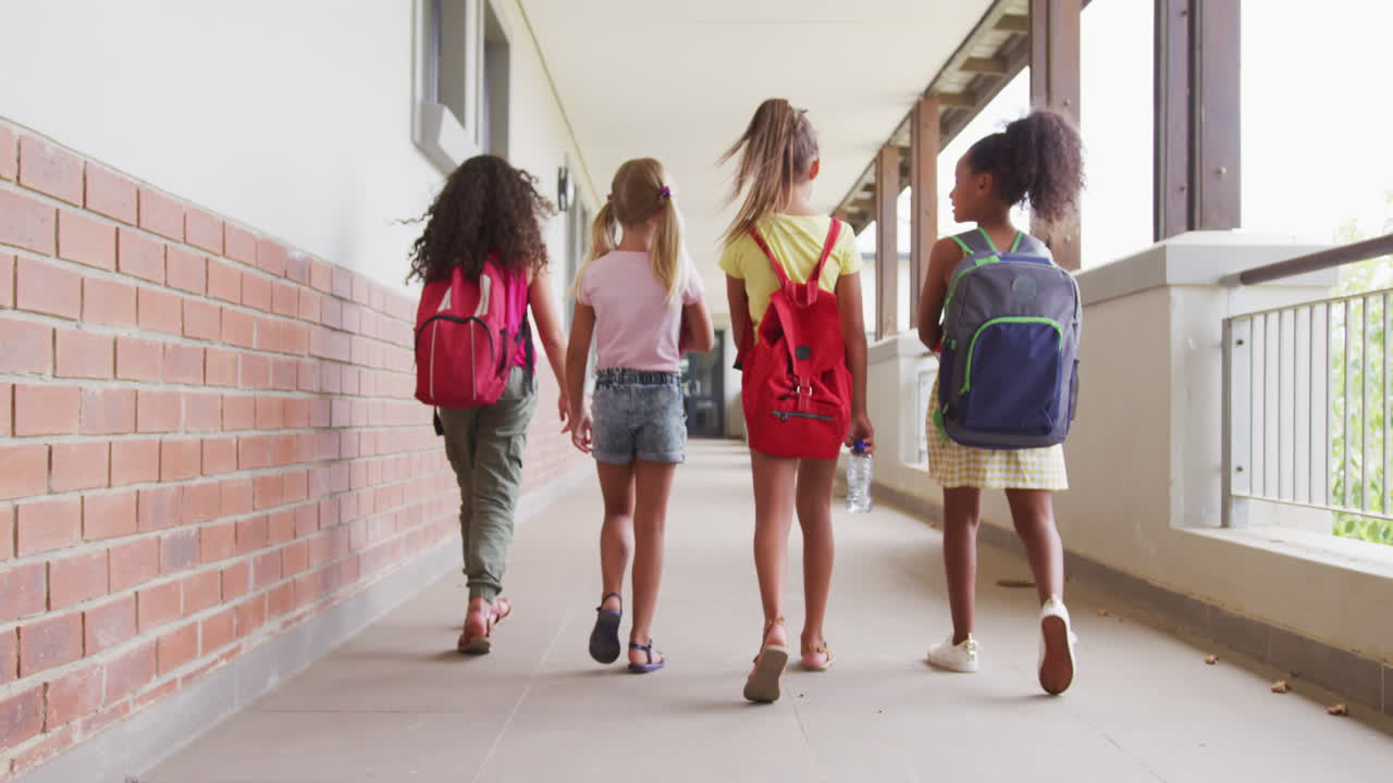 video de vista trasera de niñas diversas caminando en el pasillo de la escuela y hablando