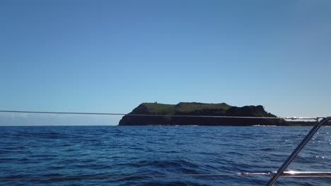 a shot from a catamaran´s port of an island with a sea lighthouse on top