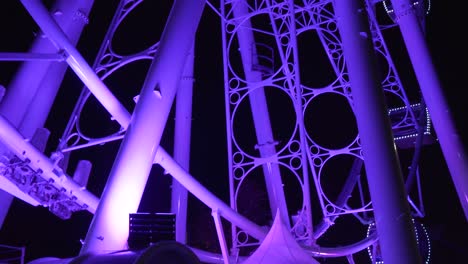 people riding a giant ferris wheel glowing with amazing purple lights - medium shot