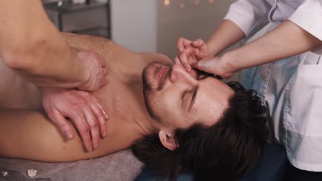 close-up therapist is giving a massage to a muscular man in a beautiful massage room while he lies on his back on a massage table receiving a two-handed massage