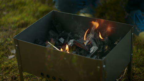 Ein-Männlicher-Camper-Beobachtet-Die-Flammen-Im-Holzkohlegrill,-Colas-Brennen-Und-Bereitet-Sich-Auf-Das-Kochen-Von-Fleisch-Vor,-Während-Er-Sich-Im-Zeltlager-Im-Wald-Ausruht