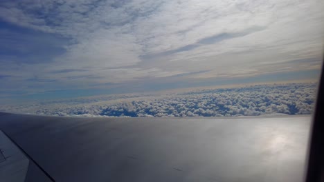 Vista-Dinámica-Del-Ala-De-Un-Avión-Volando-E-Inclinándose-Sobre-Hermosas-Nubes-Parecidas-Al-Algodón