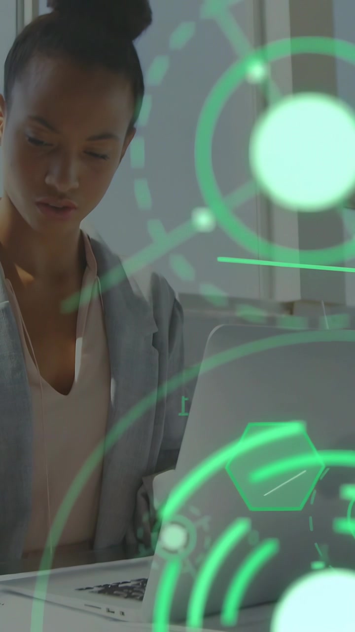 Vertikal video: Kvinde ved skrivebord studerer bærbar computer og opdaterer data, mens et grønt HUD bevæger sig over en teknologisk ramme.