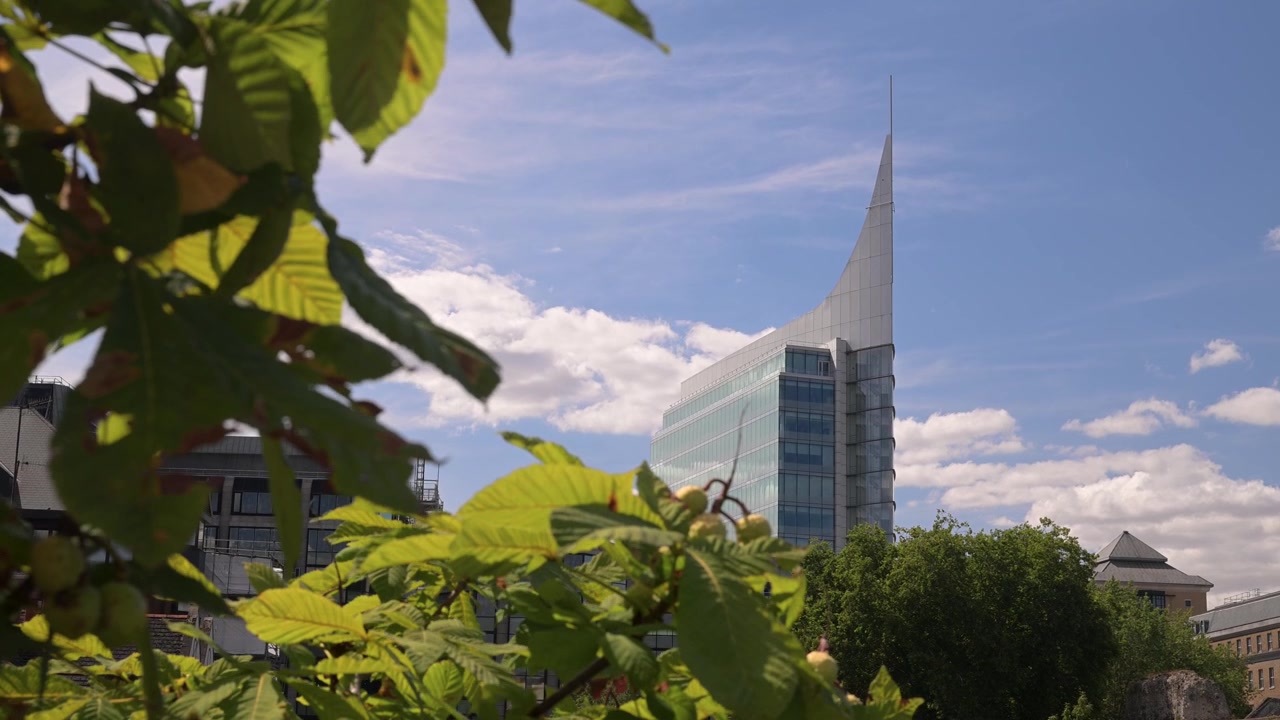 Folhas verdes em primeiro plano emolduram o edifício de escritórios The Blade contra um céu ensolarado com nuvens passageiras em Reading