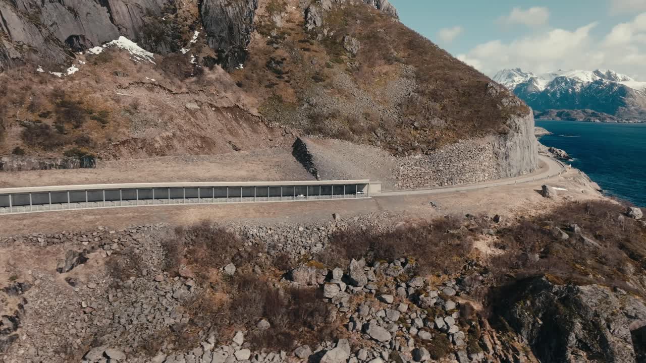 Lofoten Islands, Nordland, Norway - A Lone Car Winds its Way Along a Rugged Mountain Road, Framed by Dramatic Cliffs and Snow-capped Peaks - Tracking Shot