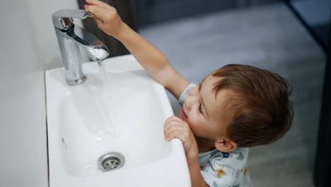 adorable baby playing with a water tap. happy toddler smiles seeing the water flow from faucet. top view.