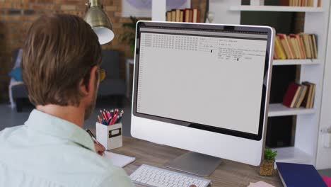 Caucasian-man-sitting-at-desk-watching-coding-data-processing-on-computer-screen