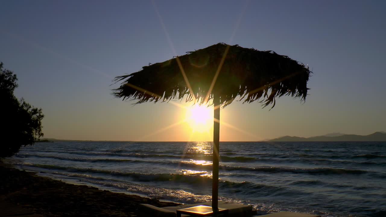 una sombrilla hecha de hojas de palma y tumbonas al atardecer en la playa de kos en el mar egeo