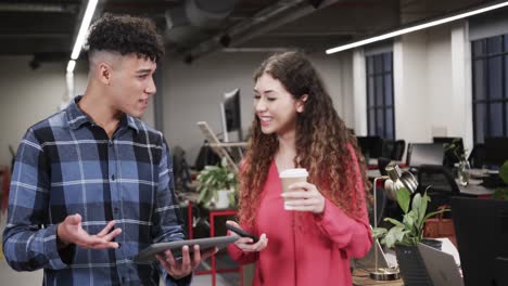 two happy diverse creative designers in discussion at tablet in casual office, slow motion