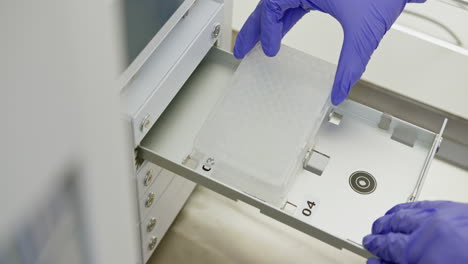 technician handling a microplate in a laboratory machine.