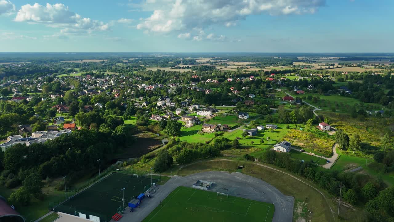Aerial drone view revealing Talsi cityscape, showcasing FC sports stadium, residential zones, verdant landscapes against bright summer sky in Latvia