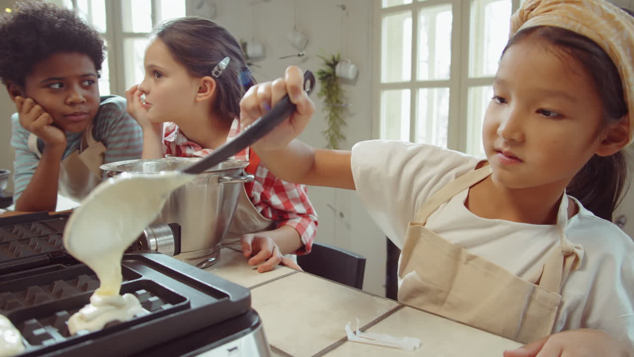 작은 아시아 소녀가 요리 마스터 클래스에 와플을 만들고 있습니다.