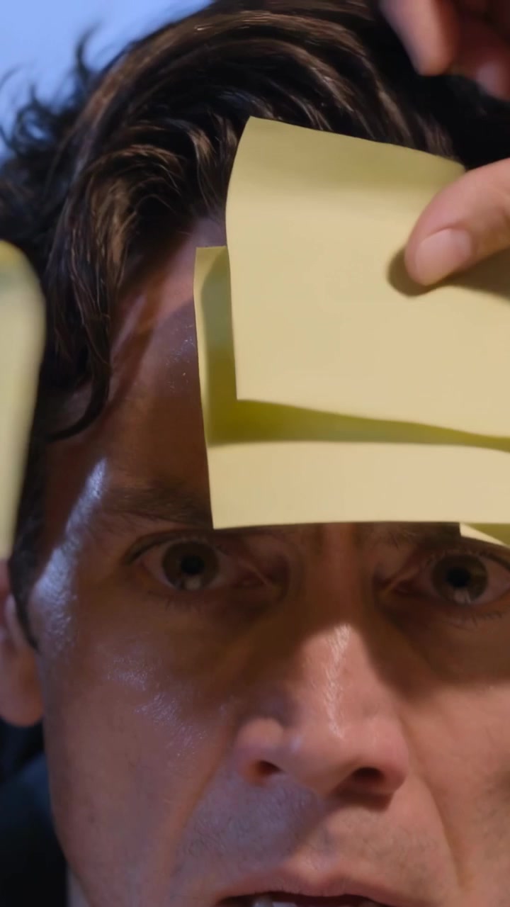 Vertical video: Entering hand placing yellow notes across man's forehead in set, man in suit, prank