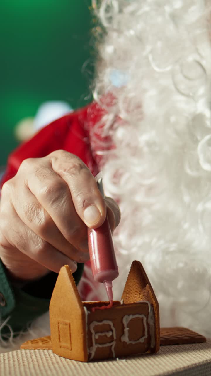 Babbo Natale che decora una casetta di pan di zenzero con la glassa.