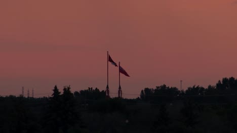 canadian and manitoban flag blowing in the winds during an orange sunrise