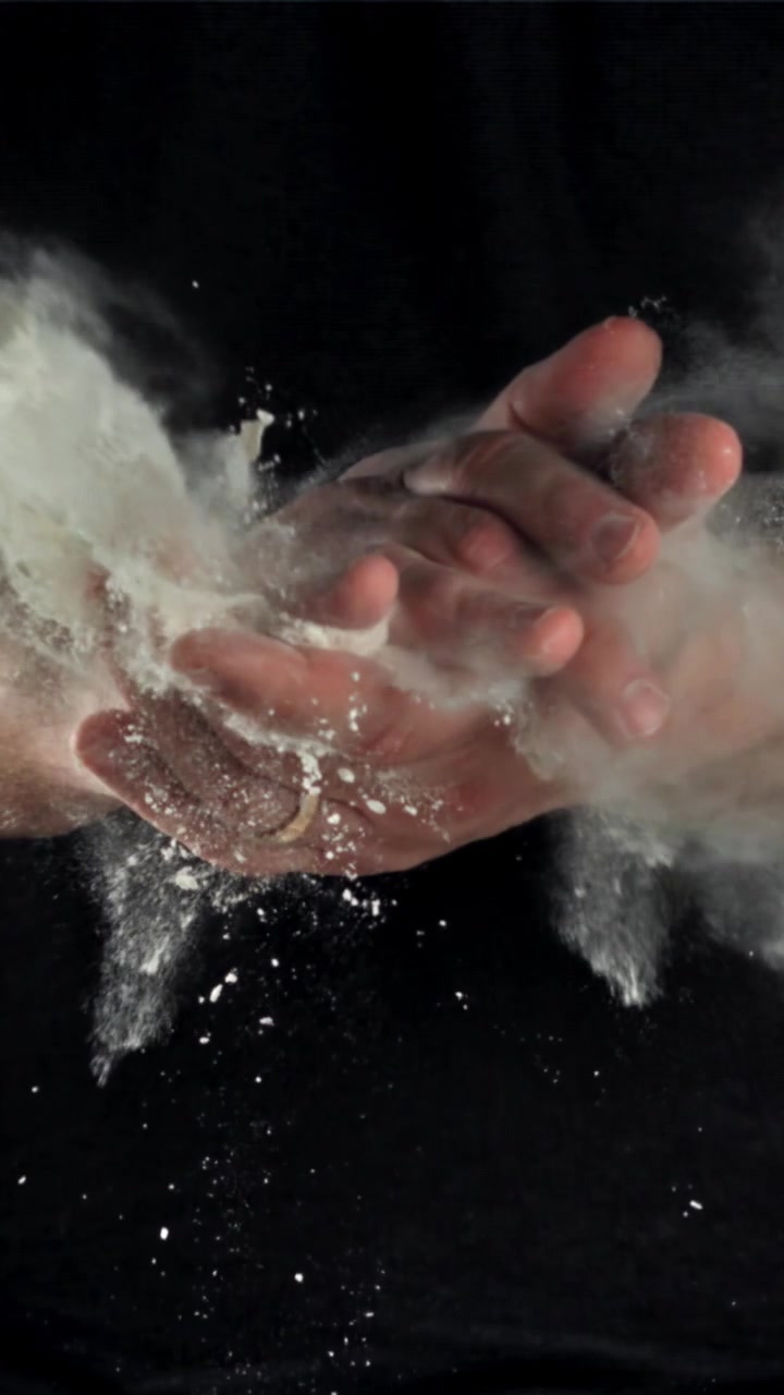 Nærbillede i slowmotion af hænder, der klapper med hvidt pulver