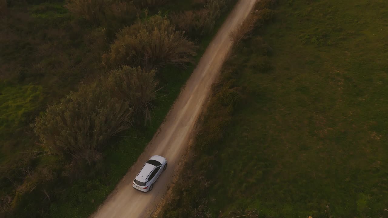 Aerial view tilting over a car driving on the coast of Magoito, sunset in Portugal