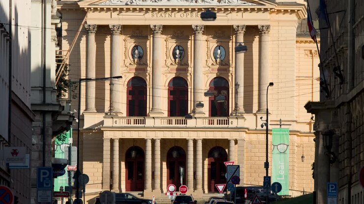 Veicoli che passano davanti alla facciata di un teatro neoclassico in pieno giorno, telecamera statica, ambiente urbano