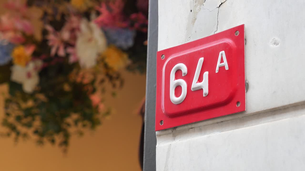 Primo piano del numero civico 64A su un cartello rosso