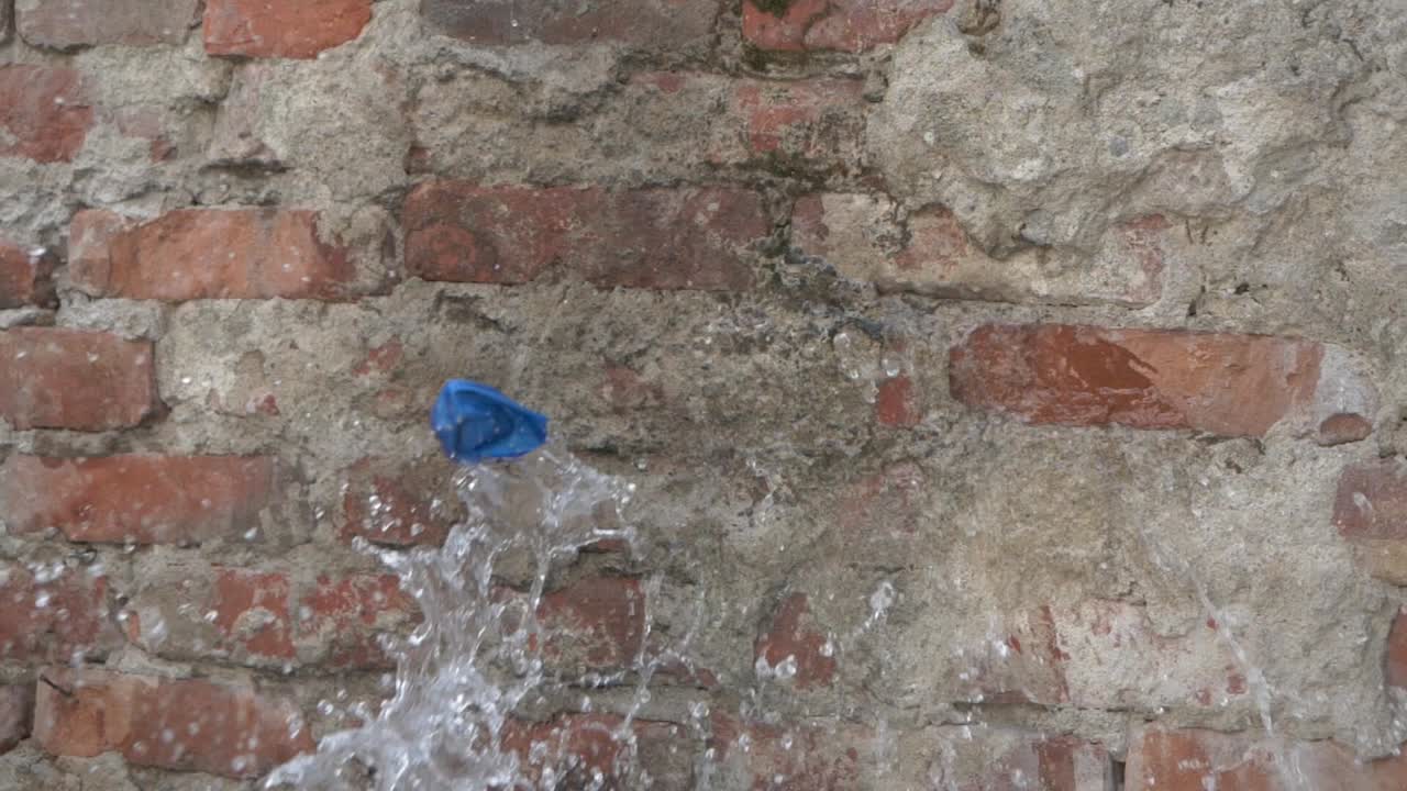 globo de agua de goma azul es arrojado a una pared de ladrillos y aparece