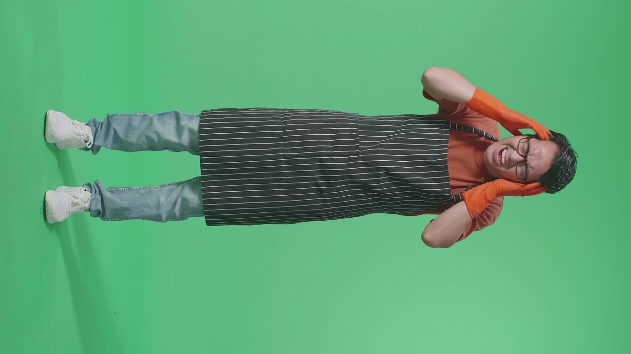 녹색 스크린 스튜디오에서 두통을 고 있는 아시아 남성 집주인의 몸이 가득 차 있습니다.