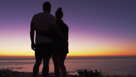 Couple-standing-and-kissing-on-a-beach-by-the-sea-at-sunset