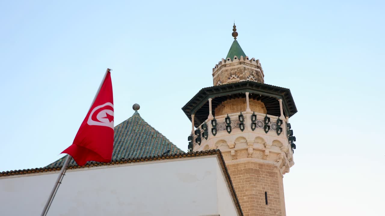 Arka planda bir kulenin cephesi ve bir duvarın bulunduğu, Tunus bayrağının alçak açıdan görünümü