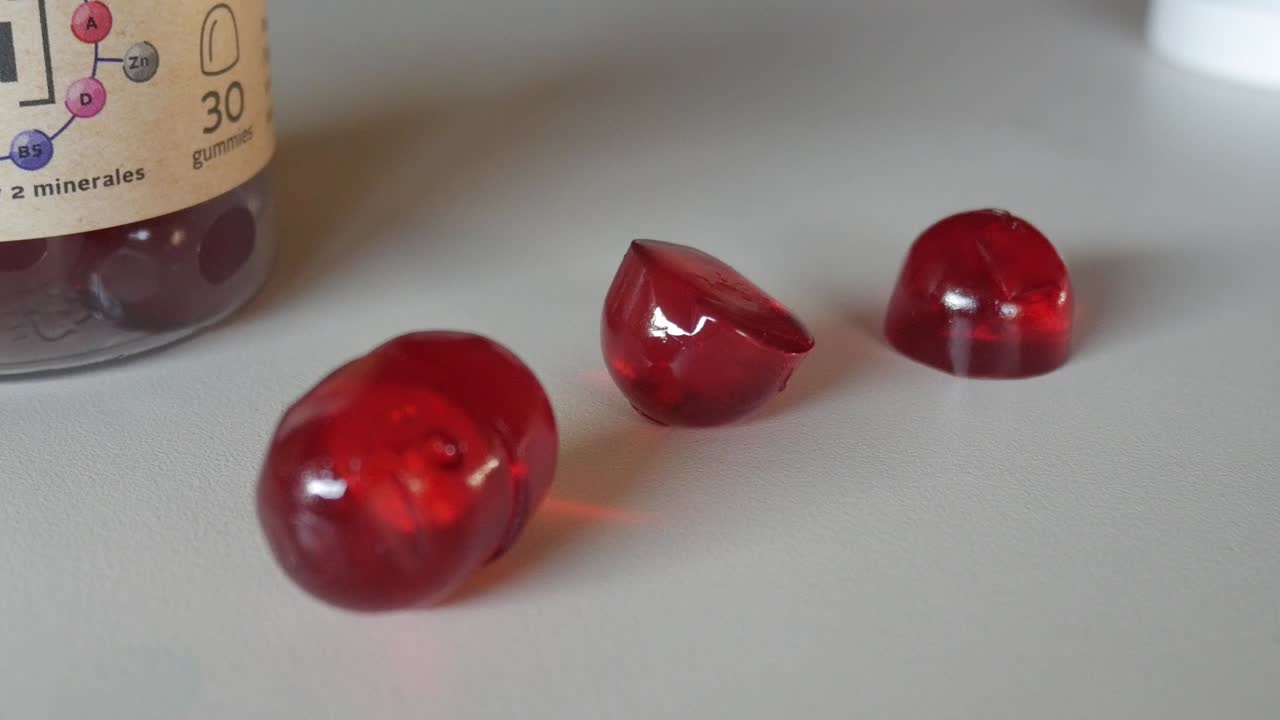 Macro close-up of red vitamin gummies on a white table showing texture and transparency under natural light