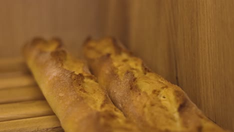 Gebackene-Lange-Baguettes-Mit-Goldener-Farbe-Auf-Holzregal-Der-Konditorei,-Aufnahme-In-Zeitlupe