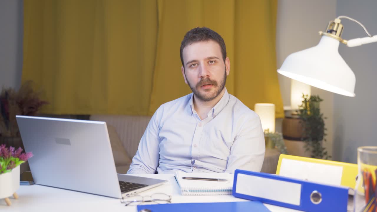 Uomo che lavora da casa con uno sguardo spento alla telecamera.