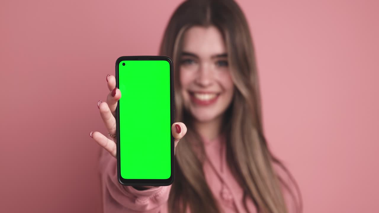 Cheerful young woman showing smartphone with chromakey