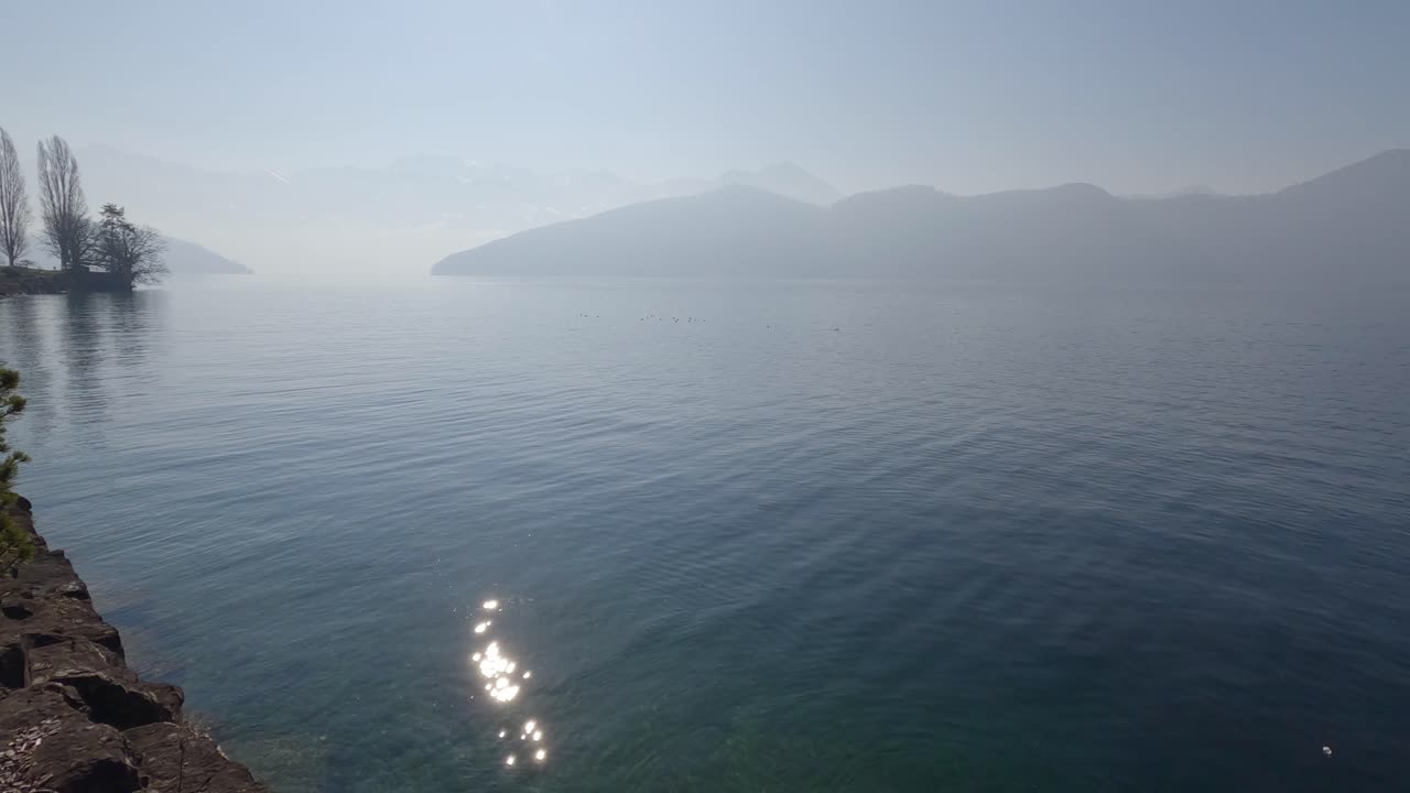 스위스 루체른 호수의 청록색 물의 전망을 드러내면서 호수 위로 열리는 산 파노라마를 패닝합니다.