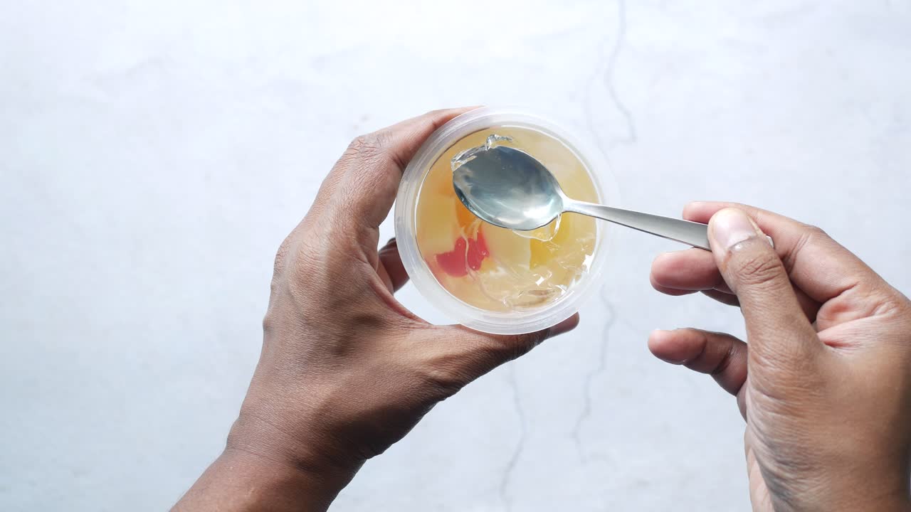 mano sosteniendo una taza transparente de jalea de fruta con una cuchara