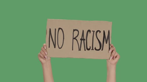 sign no racism against the background of a green screen, chroma key. hands hold poster from a cardboard box. protests peaceful protest. close up. slow motion