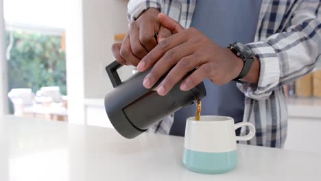 Mid-section-of-african-american-man-making-coffee-in-kitchen,-slow-motion