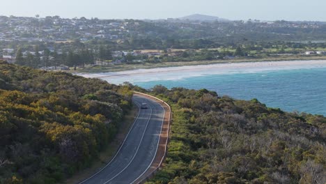 cars driving along coastal road as drone pans around at sunset