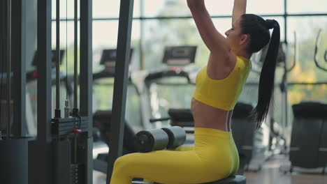 Una-Joven-Morena-Con-Traje-Amarillo-Está-Haciendo-Ejercicios-Para-Los-Músculos-De-La-Espalda-En-El-Simulador.-Una-Mujer-Hispana-Tira-De-Una-Cuerda-En-El-Simulador.-Dominadas-Simuladas