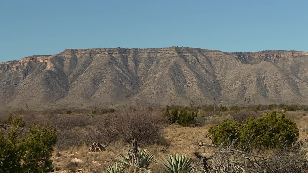 Inquadratura con zoom indietro di una cresta montuosa rocciosa sopra arbusti desertici e praterie nei Monti Guadalupe, Texas, USA.