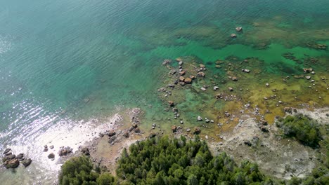 Aerial-pan-of-shallow-rocky-coastline-with-clear-blue-water,-Lake-Huron,-Michigan