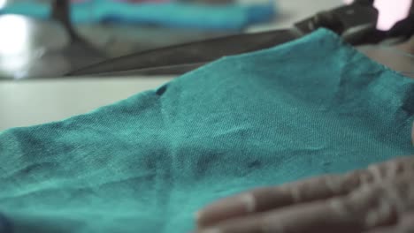 old lady tailor use scissors to cut blue fabric