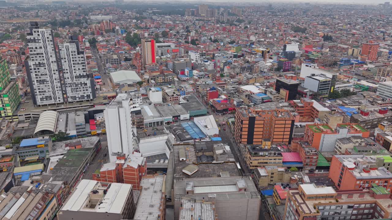 High aerial drone shot moving forward above the dense rooftops of Bogotá, showing colorful buildings, urban patterns and the vast cityscape extending into the distance