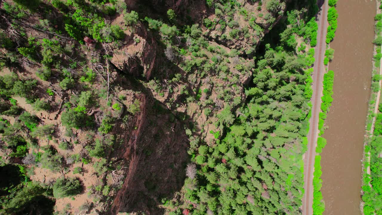 imágenes aéreas que se ciernen sobre el acantilado del cañón del desfiladero cubierto de árboles verdes brillantes y saludables cerca del río que fluye marrón en el cañón de glenwood, colorado, ee.uu.