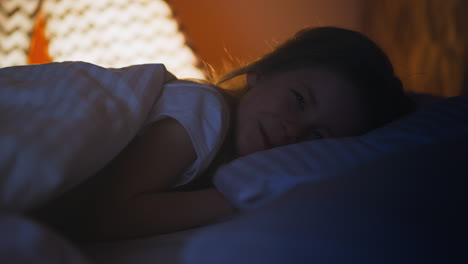 little girl smiles to camera under soft blanket on bed