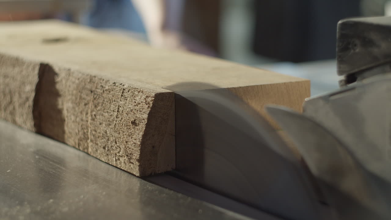 High quality video of a saw blade cutting through solid timber in a warm, cinematic workshop atmosphere with dust in the air and soft light highlighting the wood texture